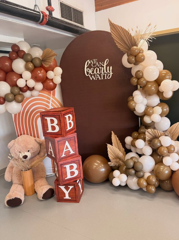 Teddy bear baby shower with a brown arch backdrop, balloon garlands, BABY blocks and a plush bear